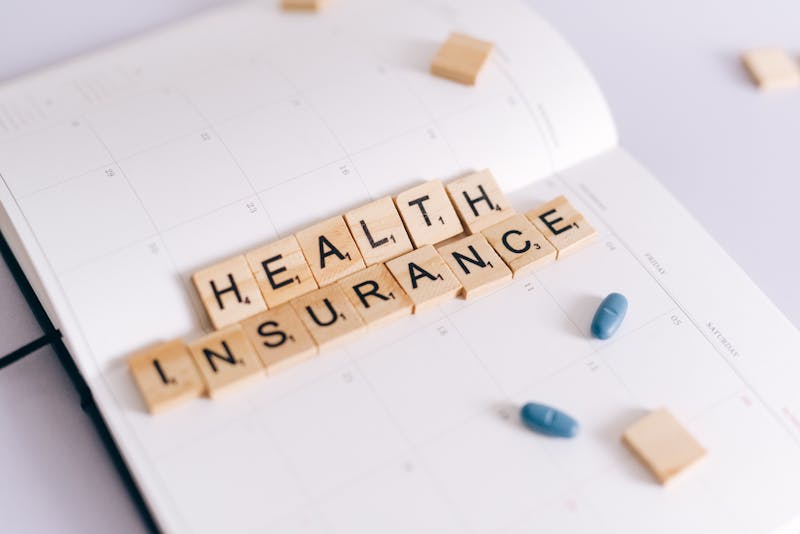 Tessere Scrabble che compongono la scritta Health Insurance accanto a medicinali e un planner
