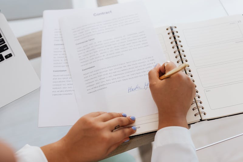 Hands signing a legal contract on a desk with office supplies